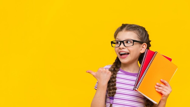 The little girl points her finger to the side and smiles A schoolgirl with pigtails and glasses on an isolated background