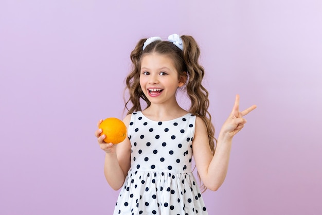 A little girl in a polka dot dress holds an orange and shows a bunny Vitamins for children