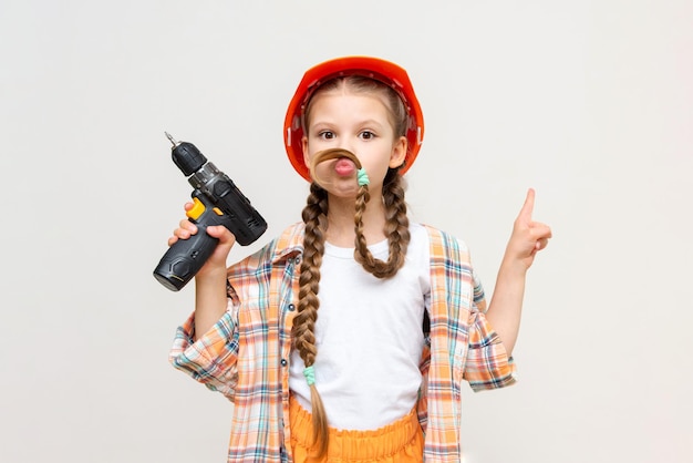 A little girl portrays her father by making a mustache out of her hair A child with a drill and a protective construction helmet on a white isolated background