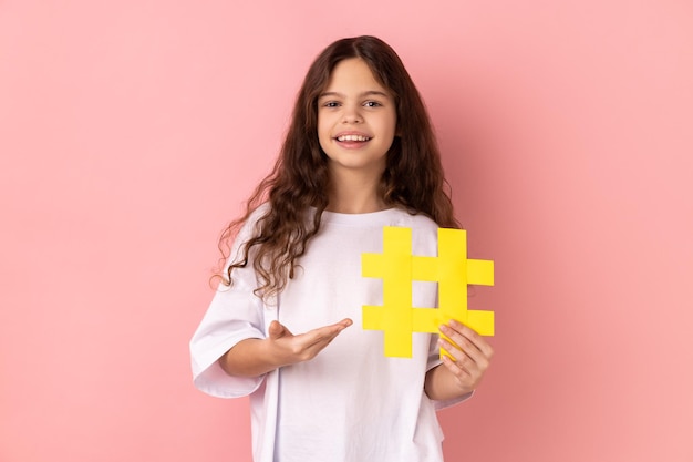 Little girl presenting big yellow hashtag symbol and smiling at camera blogging and child content