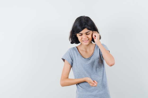 Little girl pretending to talk on mobile phone in t-shirt and looking pensive , front view.