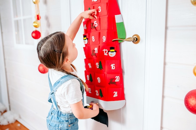 Little girl pulls out a gift from a red advent calendar at home