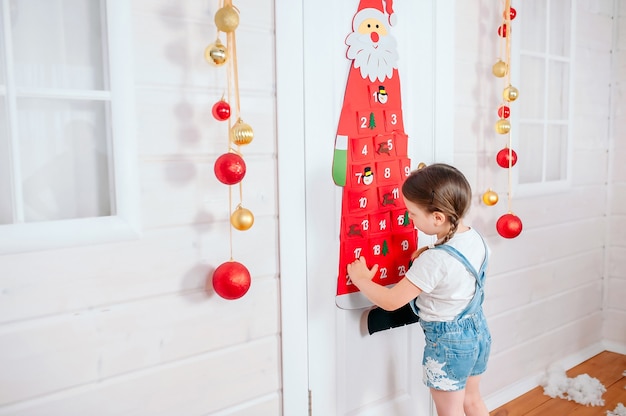 Little girl pulls out a gift from a red advent calendar at home