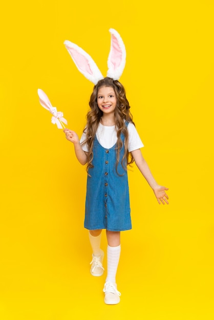 A little girl in a rabbit costume A child with long ears on his head celebrates spring Easter Children's holiday A little girl in full height on a yellow isolated background