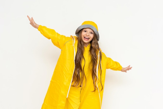 A little girl in a raincoat has spread her arms in different directions and is smiling broadly A child in a yellow raincoat and panama hat on a white isolated background