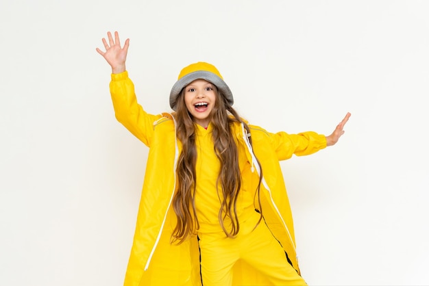 A little girl in a raincoat has spread her arms in different directions and is smiling broadly A child in a yellow raincoat and panama hat on a white isolated background