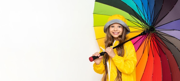 A little girl in a raincoat holds a multicolored umbrella on a white isolated background Rainy weather copy space