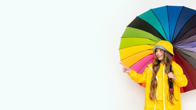 A little girl in a raincoat holds a multicolored umbrella on a white isolated background Rainy weather copy space