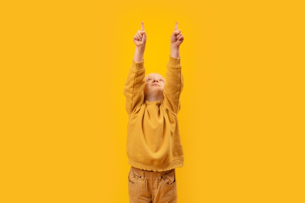 Little girl raised hands up and points index fingers up Copy space mock up Vertical frame child in yellow clothes