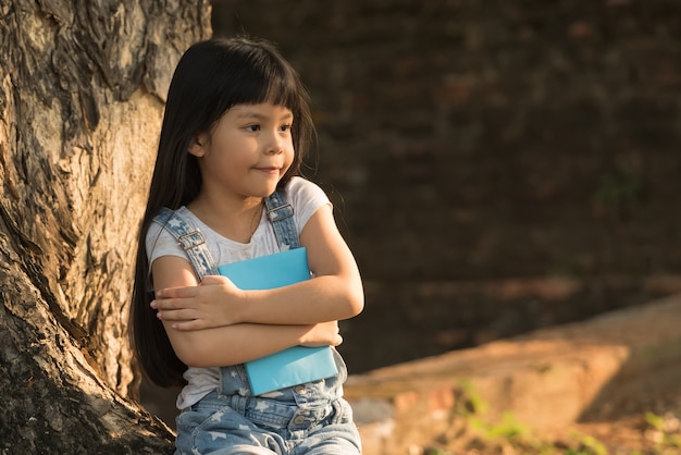 Little girl reading a book under big tree