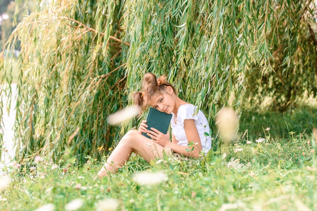 Little girl reading a book with her friend puppy dog in the outdoors.