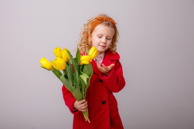 A little girl in a red coat holds a bouquet of spring tulip flowers on a white background