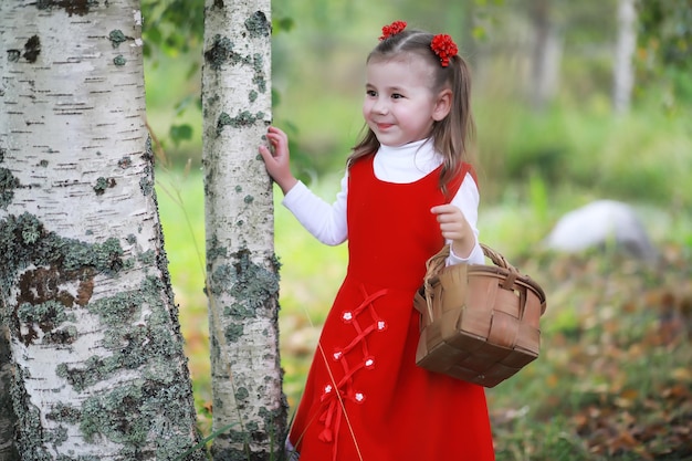 A little girl in a red hat and dresses is walking in the park Cosplay for the fairytale hero Little Red Riding Hood