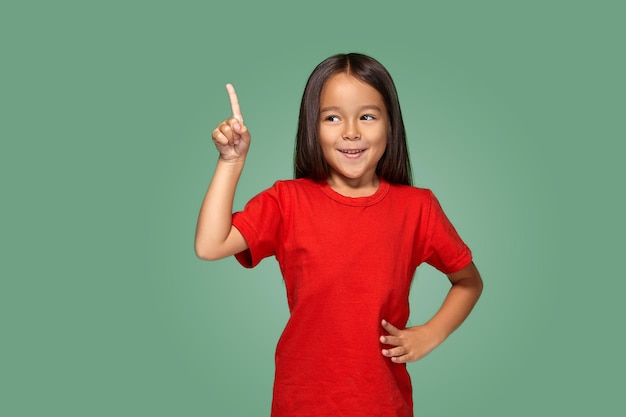 Little girl in red t-shirt with finger up on a green background