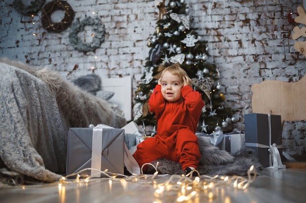 Photo a little girl in a red warm sweater sits under a christmas tree with toys and gifts. happy childhood. new year holiday atmosphere