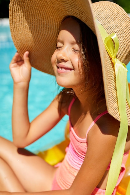 Little girl relaxing in swimming pool, enjoying suntan on inflatable yellow mattress