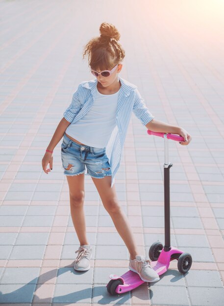 Little girl riding scooter outdoors. Street urban scenery