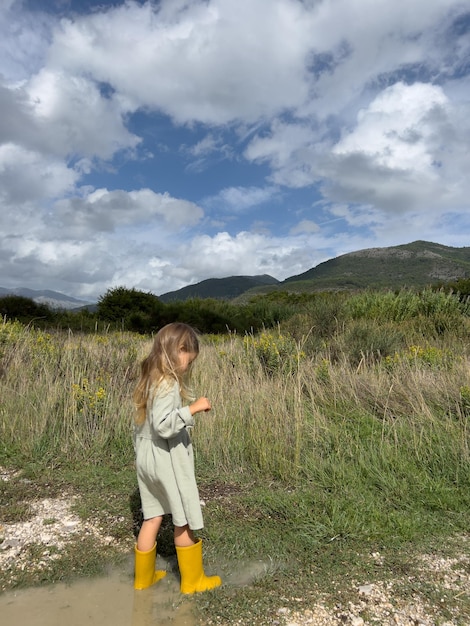 Little girl in rubber boots walks through puddles in a mountain valley