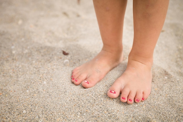 Little girl's legs and feet walking on the sand of the beach with the sea water in the background