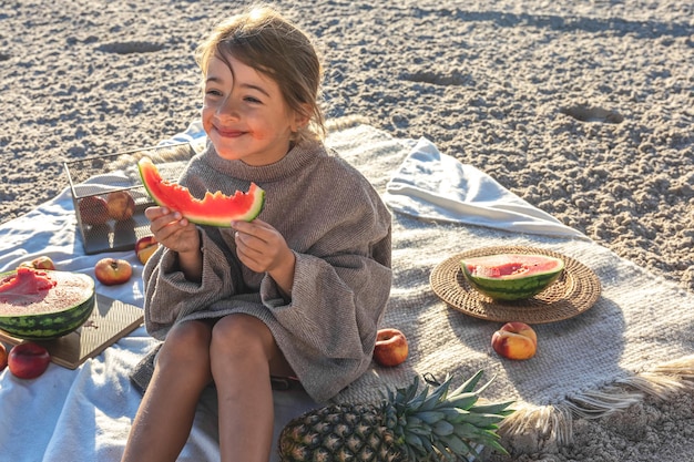 A little girl on a sandy sea beach eats a watermelon