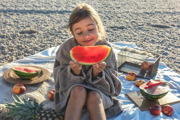 A little girl on a sandy sea beach eats a watermelon