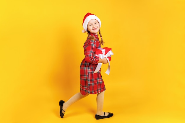 Little girl in santa claus hat sneaks with christmas present.