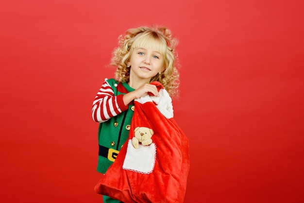 Little girl in Santa elf helper costume on bright red vivid color background.