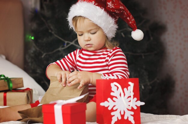 Little girl in Santa hat opening Christmas gift box Funny and expressive toddler enjoying gifts