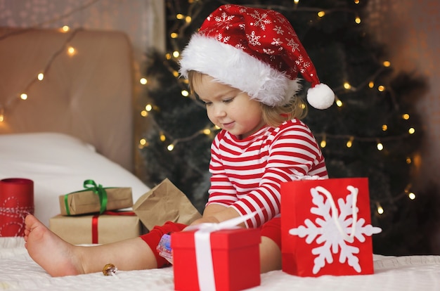 Little girl in Santa hat opening Christmas gift box Funny and expressive toddler enjoying gifts