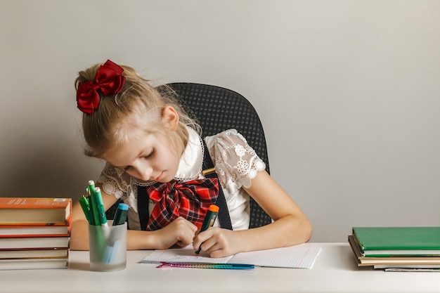 A little girl in a school uniform draws in a notebook with her left hand