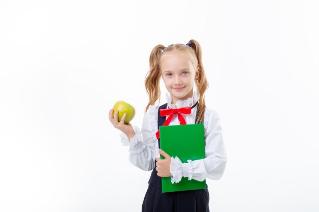 A little girl in a school uniform holds a book and an apple isolated on a white background