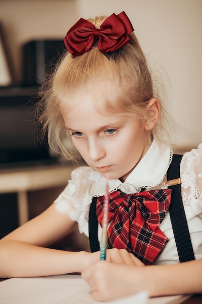 A little girl in a school uniform writes in a notebook with her left hand does homework at home