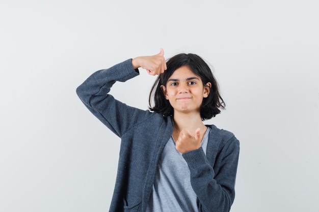 Little girl showing double thumbs up in t-shirt, jacket and looking confident. front view.