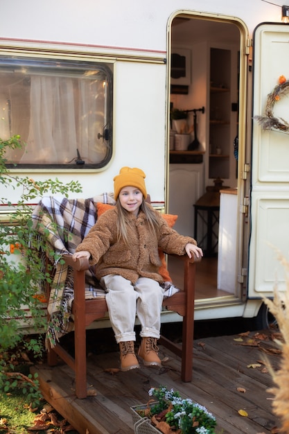 little girl sit on porch RV campsite house with chrysanthemum potted and pumpkins in autumn garden