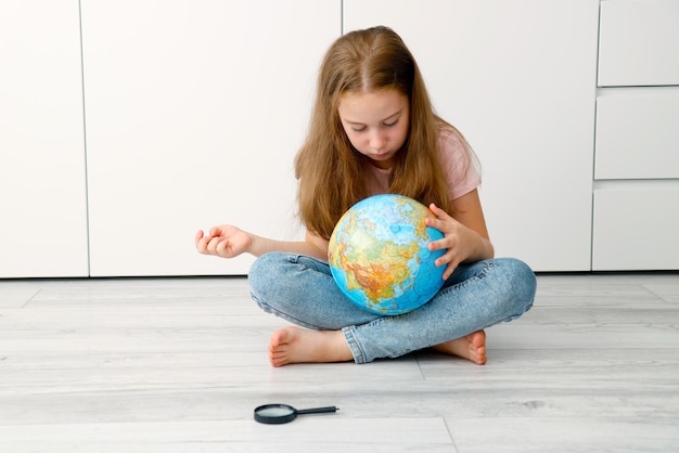 a little girl sits on the floor and carefully looks at the globe a magnifying glass lies next to her