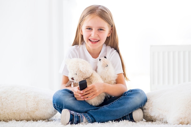 Little girl sits on floor holding plush toys and tv remote