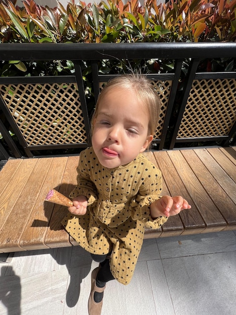 Little girl sits licking her lips with an ice cream cone in her hand