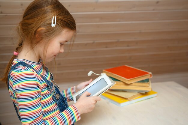 little girl sits at a table and reads an e-book.