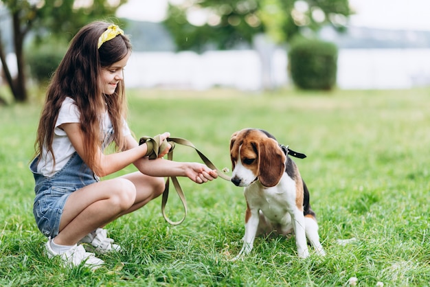 A little girl sits with a dog and gives her a sniff of a flower.