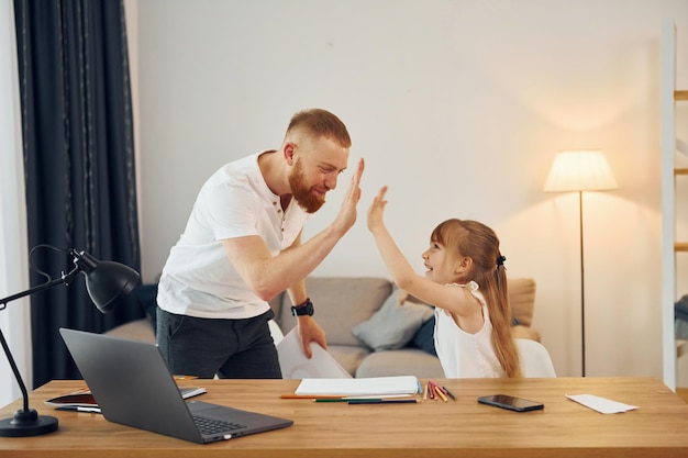 Little girl sitting by the table Father with his little daughter is at home together