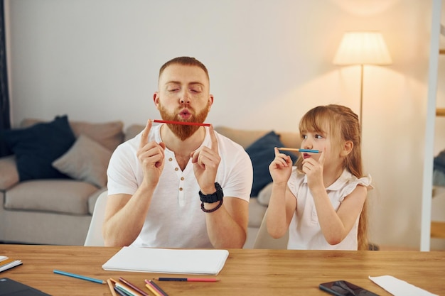 Little girl sitting by the table Father with his little daughter is at home together