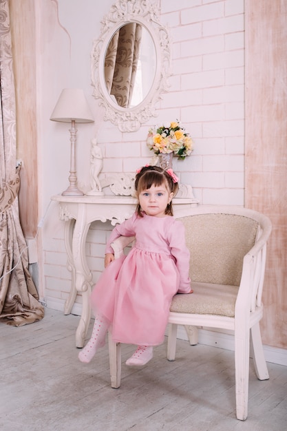 Little girl sitting on chair in pink dress at home