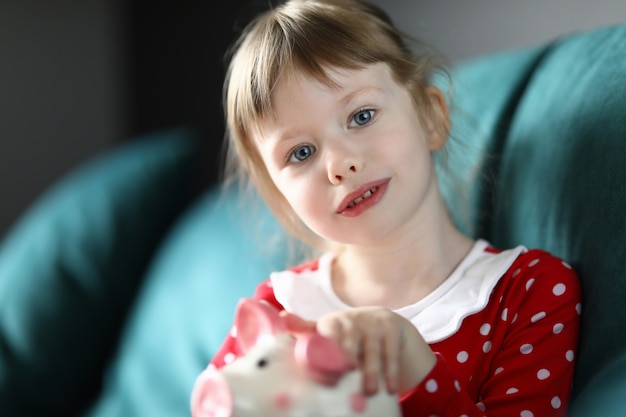 Little girl sitting at home sofa with piggy bank