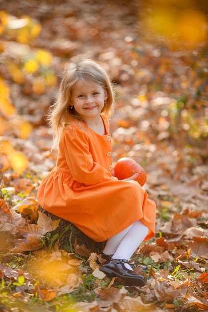 Little girl sitting in the Park in autumn holding a pumpkin for Halloween