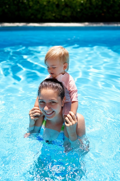 Little girl sitting on the shoulders of her mother standing in the pool