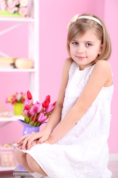 Little girl sitting on small ladder with flowers on pink background