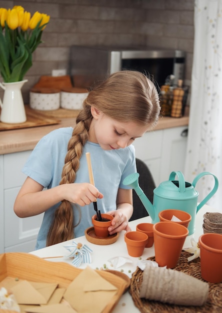 Little girl sitting at the table at home sowing seeds into flower pots Home gardening