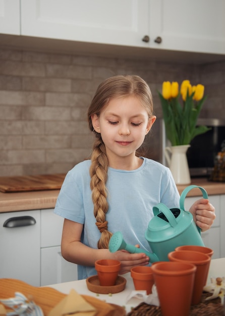 Little girl sitting at the table at home sowing seeds into flower pots Home gardening