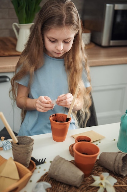 Little girl sitting at the table at home sowing seeds into flower pots