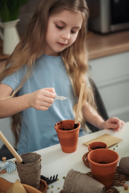 Little girl sitting at the table at home sowing seeds into flower pots